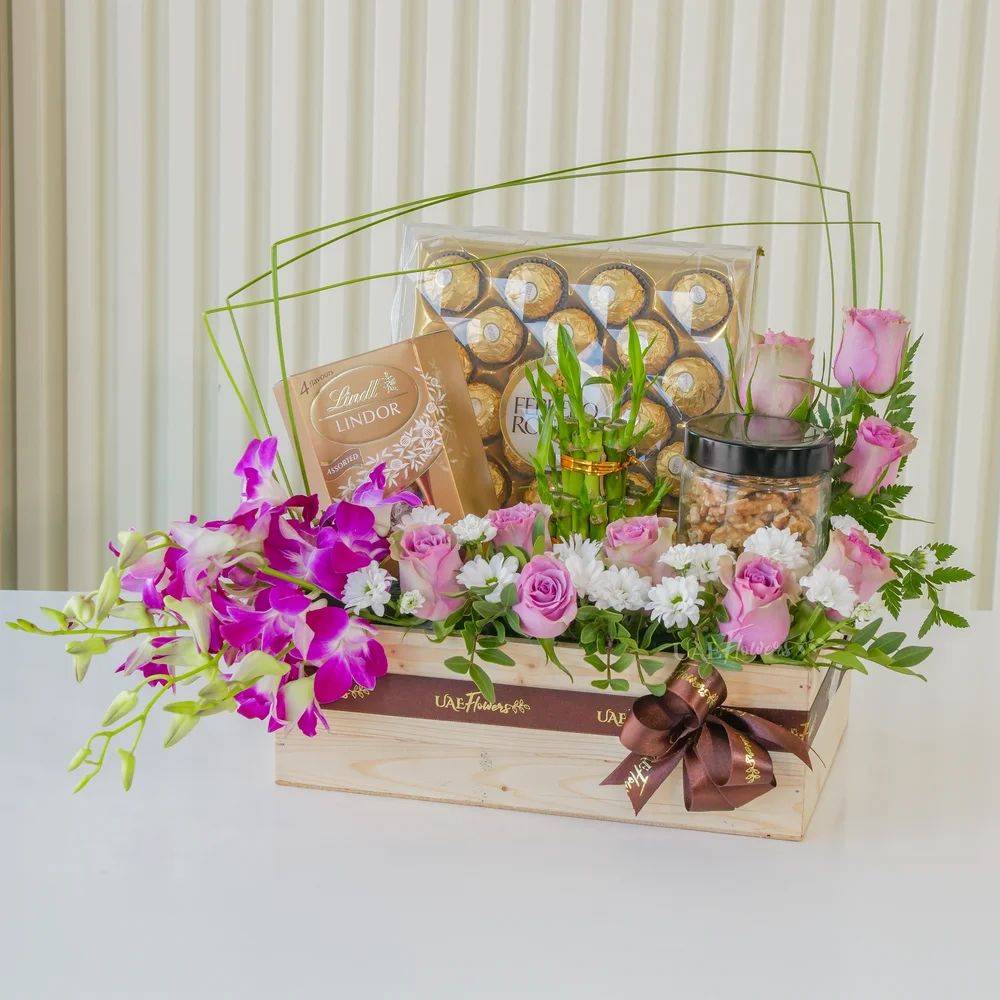 A wooden box arrangement of 10 pink roses, 5 purple orchids, white chrysanthemums, 250Gms of walnut in jar, 2 layer lucky bamboo, 24pcs of ferrero rocher chocolate and lindt lindor assorted chocolate box 200gms with green fillers.