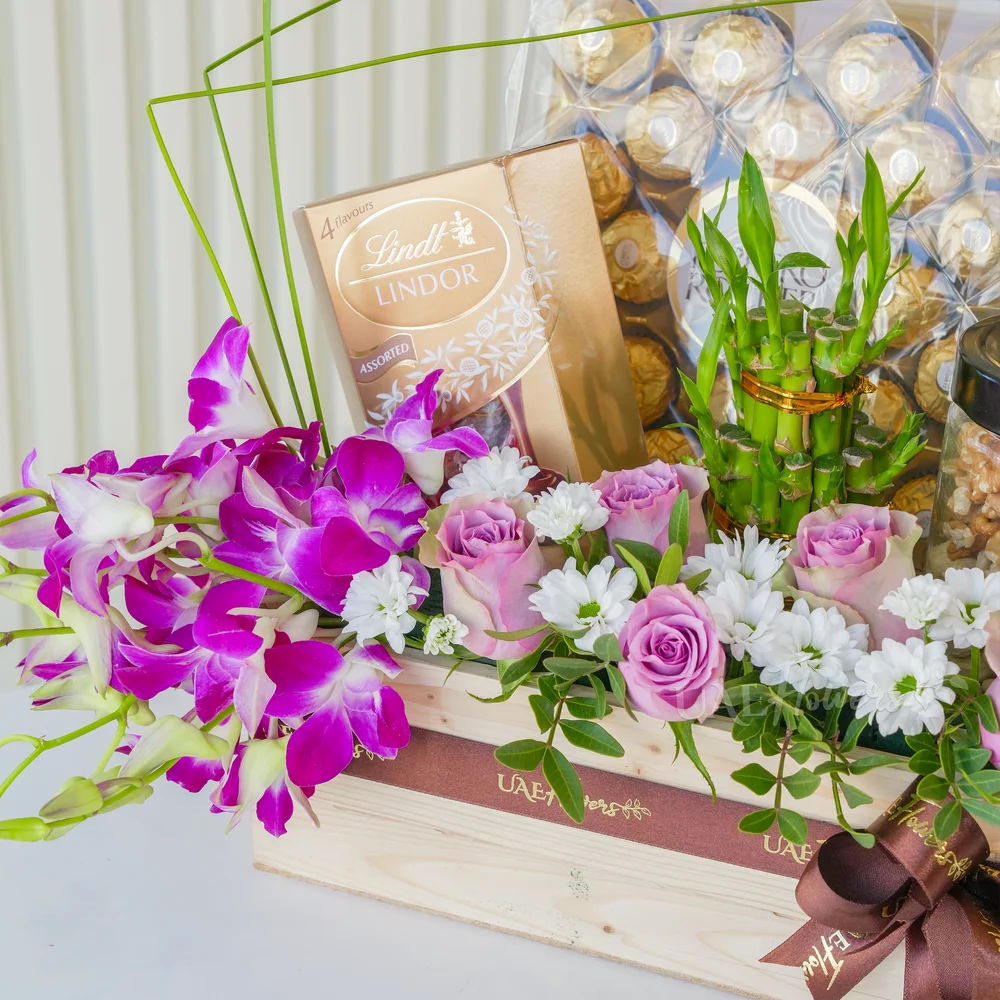 A wooden box arrangement of 10 pink roses, 5 purple orchids, white chrysanthemums, 250Gms of walnut in jar, 2 layer lucky bamboo, 24pcs of ferrero rocher chocolate and lindt lindor assorted chocolate box 200gms with green fillers.