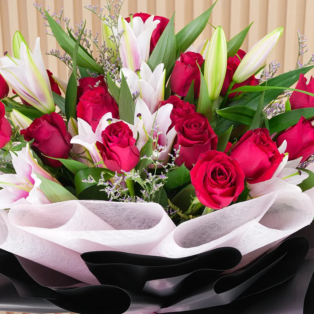 A bouquet of 4 pink lilies & 10 red roses in pink wrapping paper tied with a pink ribbon