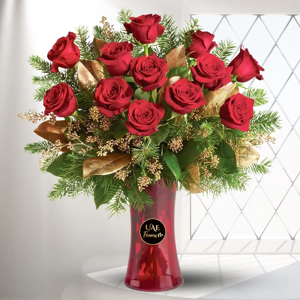 12 red roses with green and golden fir branches in a radiantly red glass vase