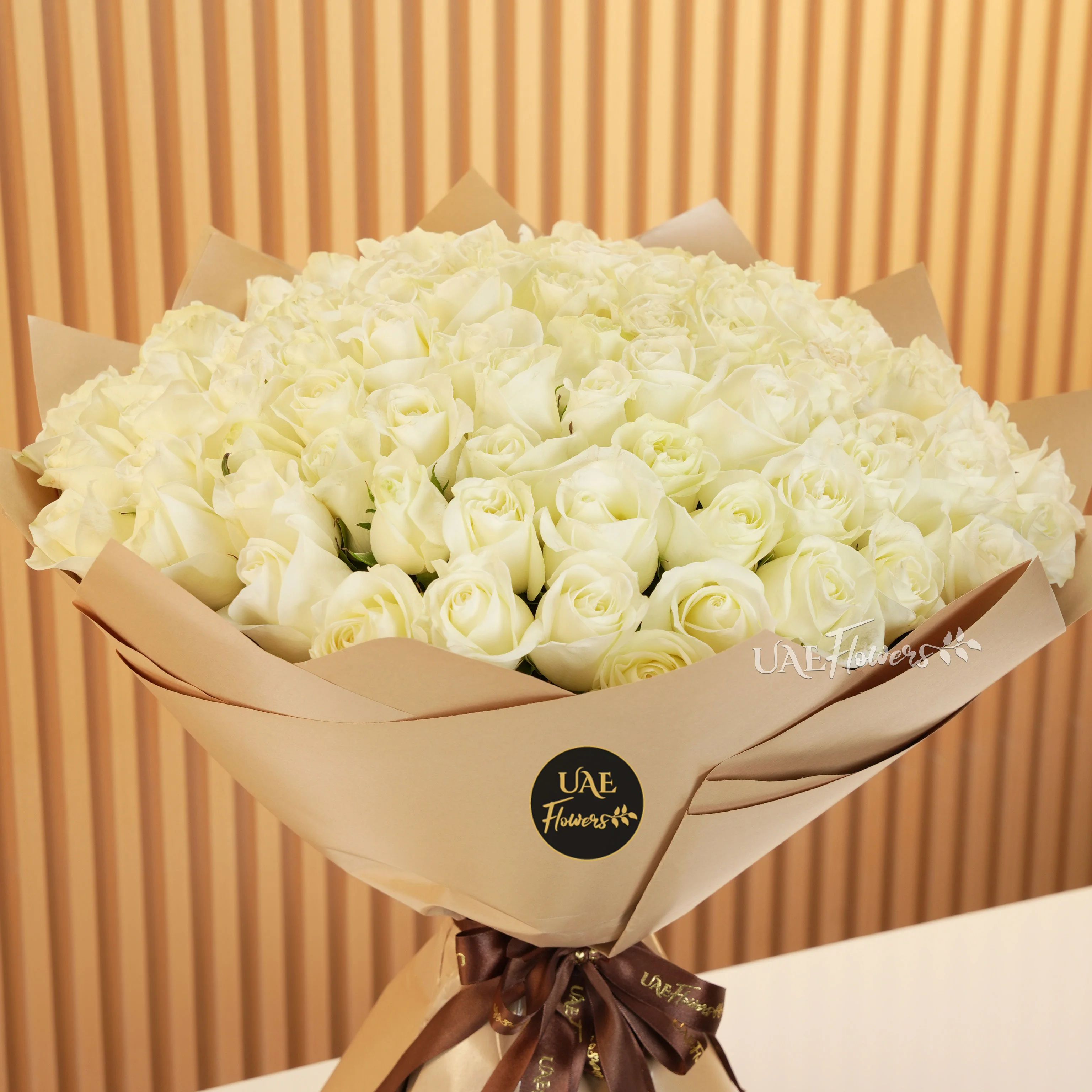 A bouquet of 100 white roses in brown wrapping paper tied with brown ribbons