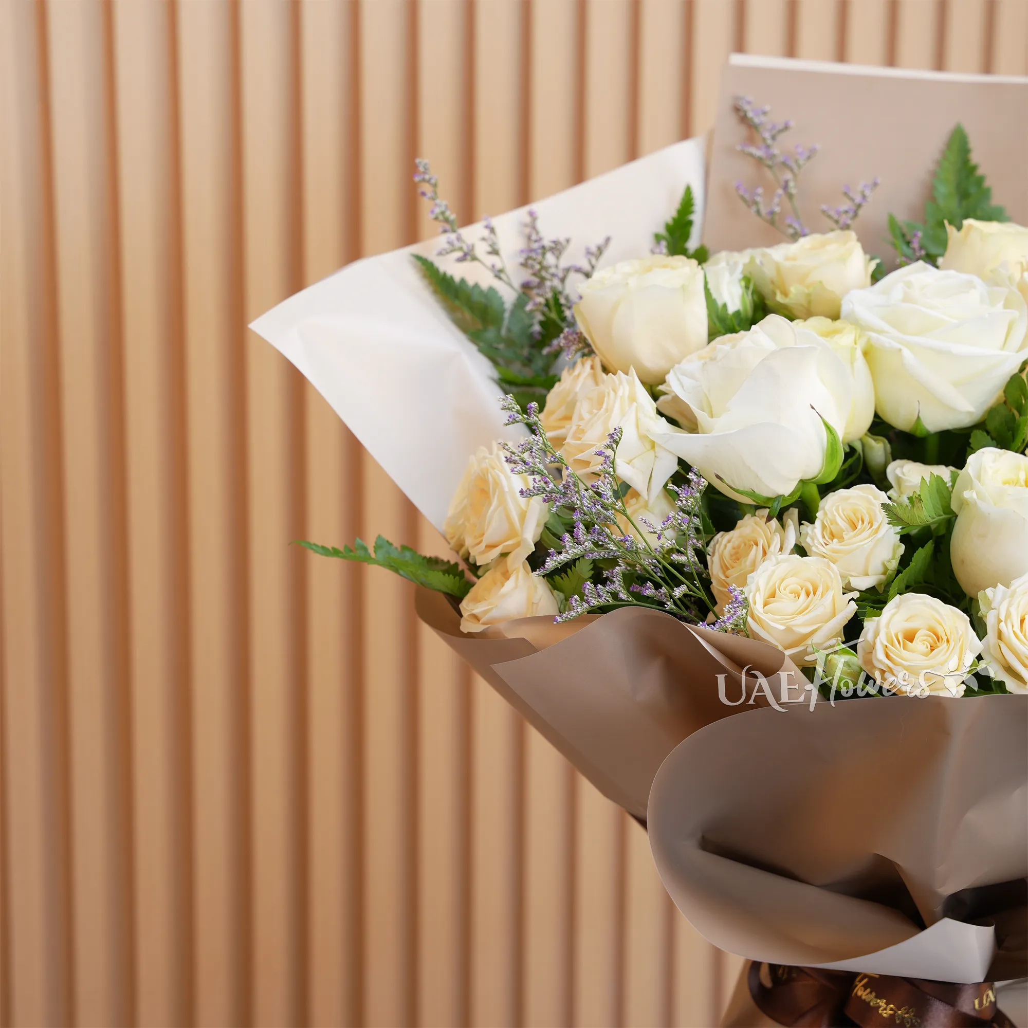 Bouquet of 8 white and peach roses with 2 peach spray roses and green fillers, wrapped in paper and tied with ribbons.
