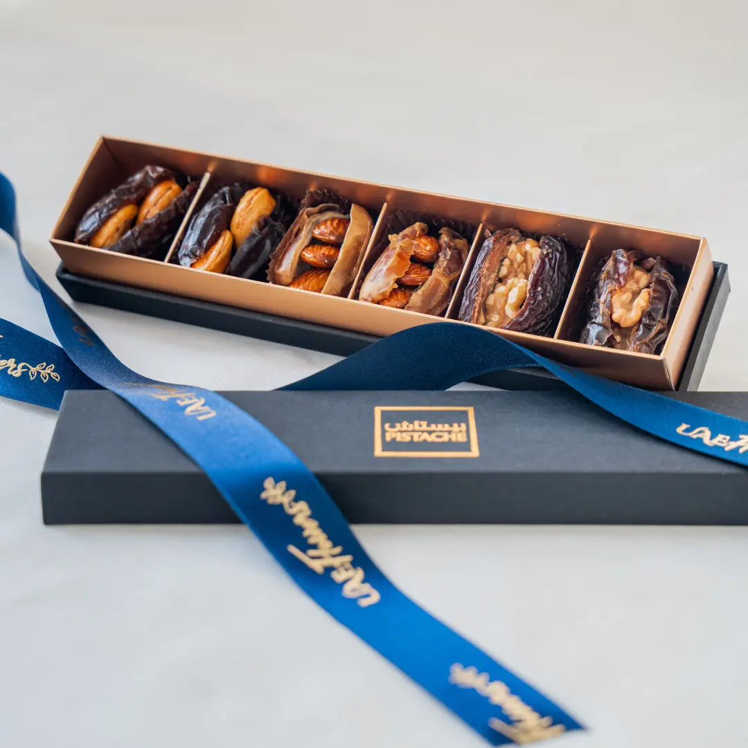 A six-piece premium stuffed dates assortment arranged in a luxury matte black and gold gift box with a branded UAE Flowers satin ribbon.