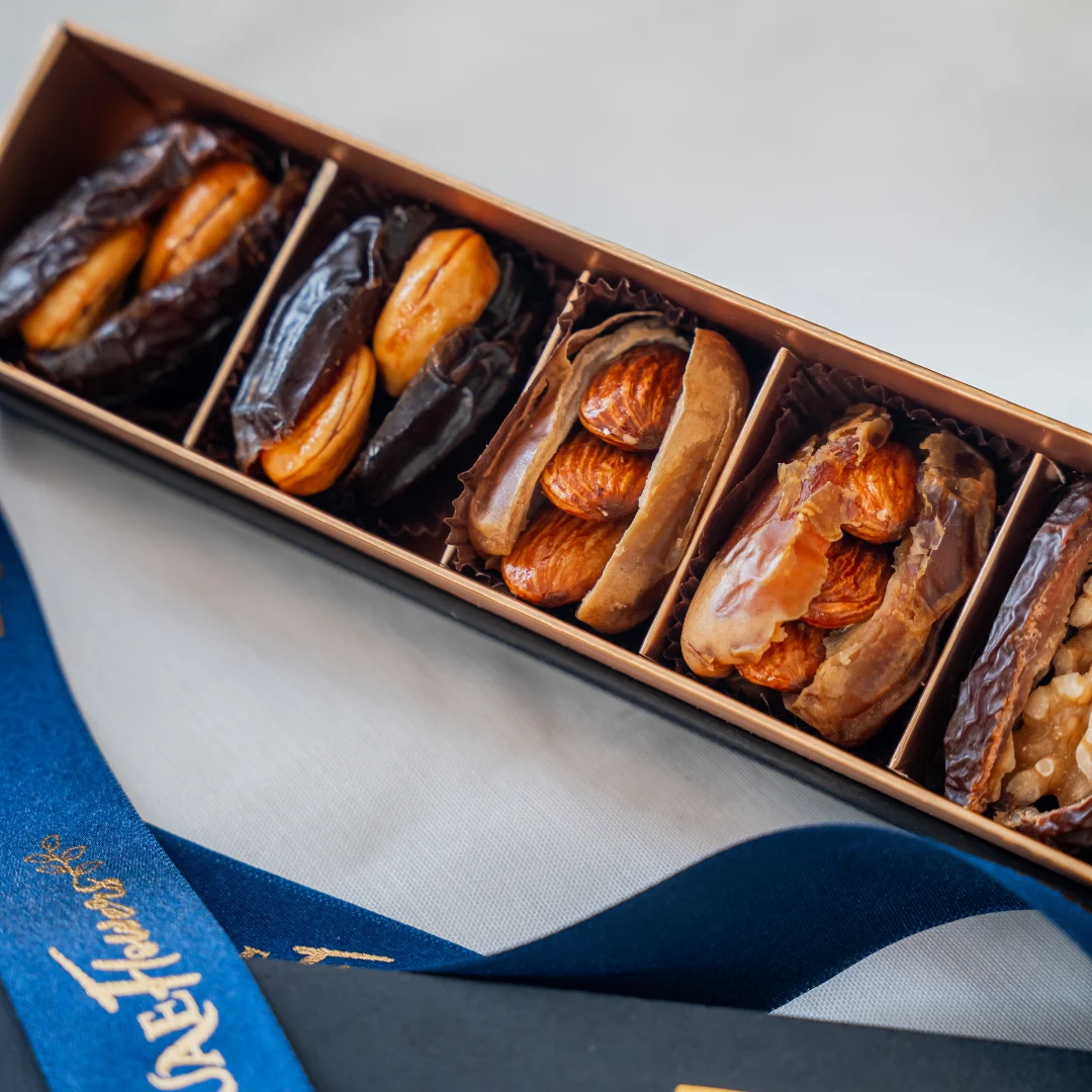 A six-piece premium stuffed dates assortment arranged in a luxury matte black and gold gift box with a branded UAE Flowers satin ribbon.