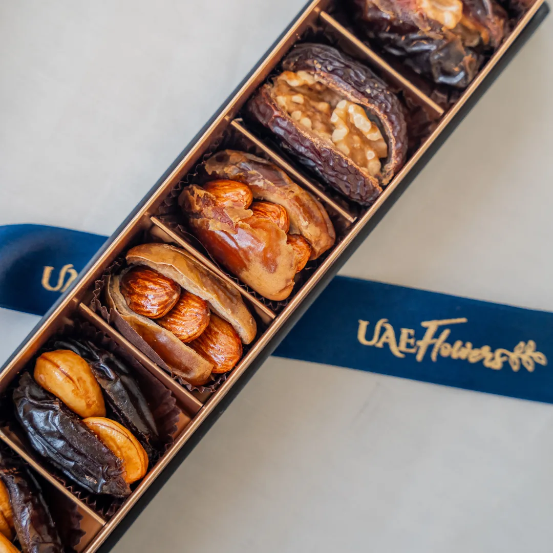 A six-piece premium stuffed dates assortment arranged in a luxury matte black and gold gift box with a branded UAE Flowers satin ribbon.