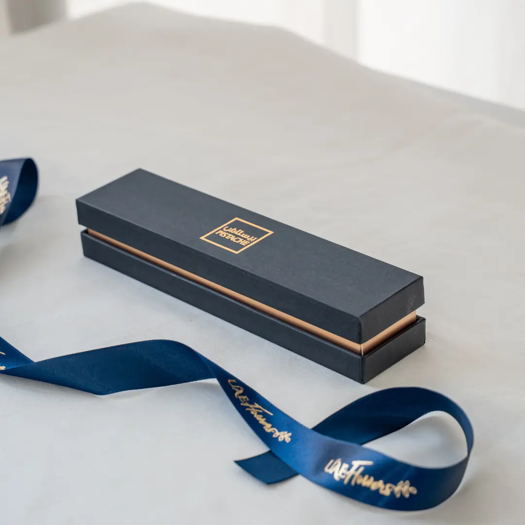 A six-piece premium stuffed dates assortment arranged in a luxury matte black and gold gift box with a branded UAE Flowers satin ribbon.