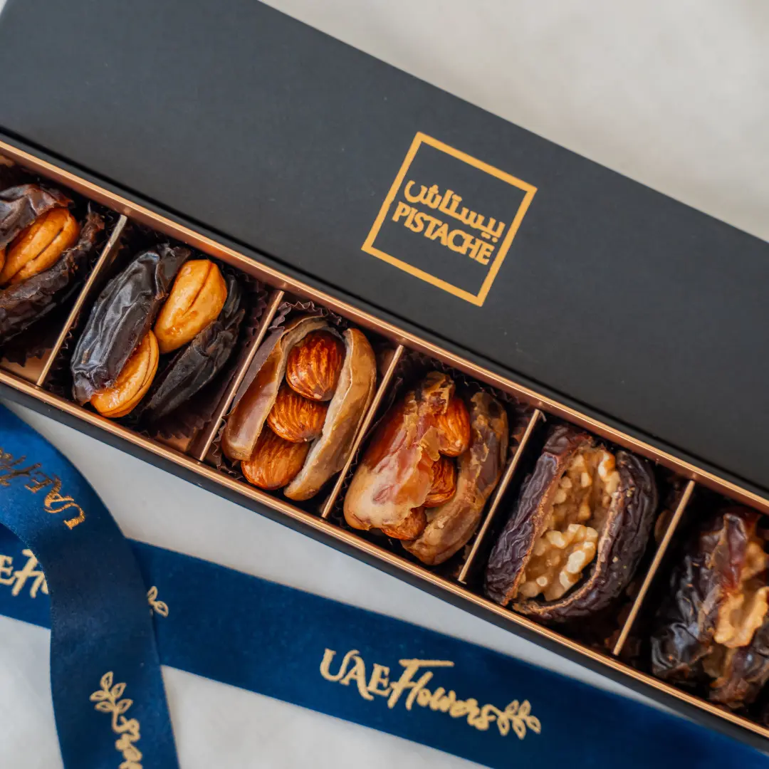 A six-piece premium stuffed dates assortment arranged in a luxury matte black and gold gift box with a branded UAE Flowers satin ribbon.