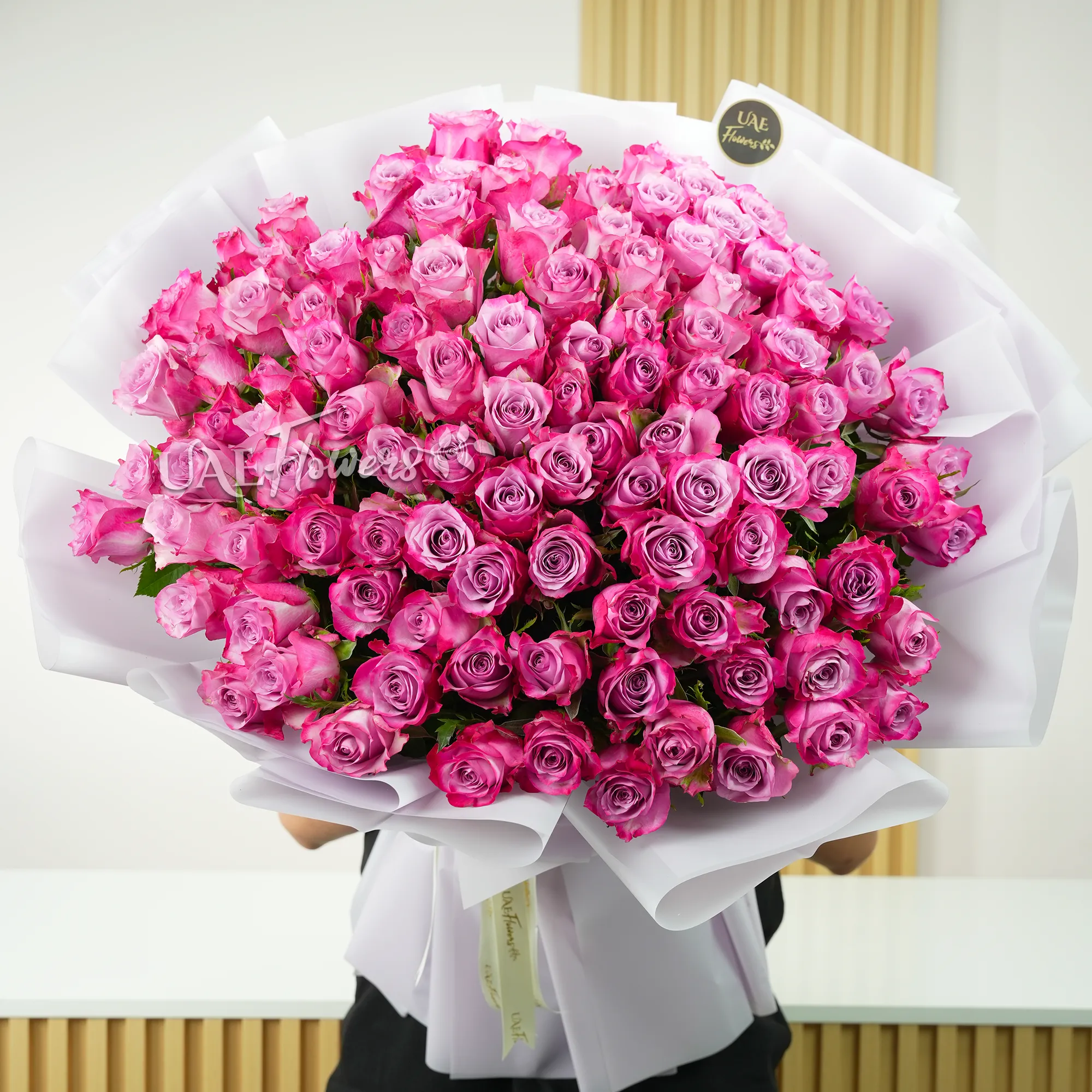100 purple roses with fillers, wrapped in white paper and tied with ribbons
