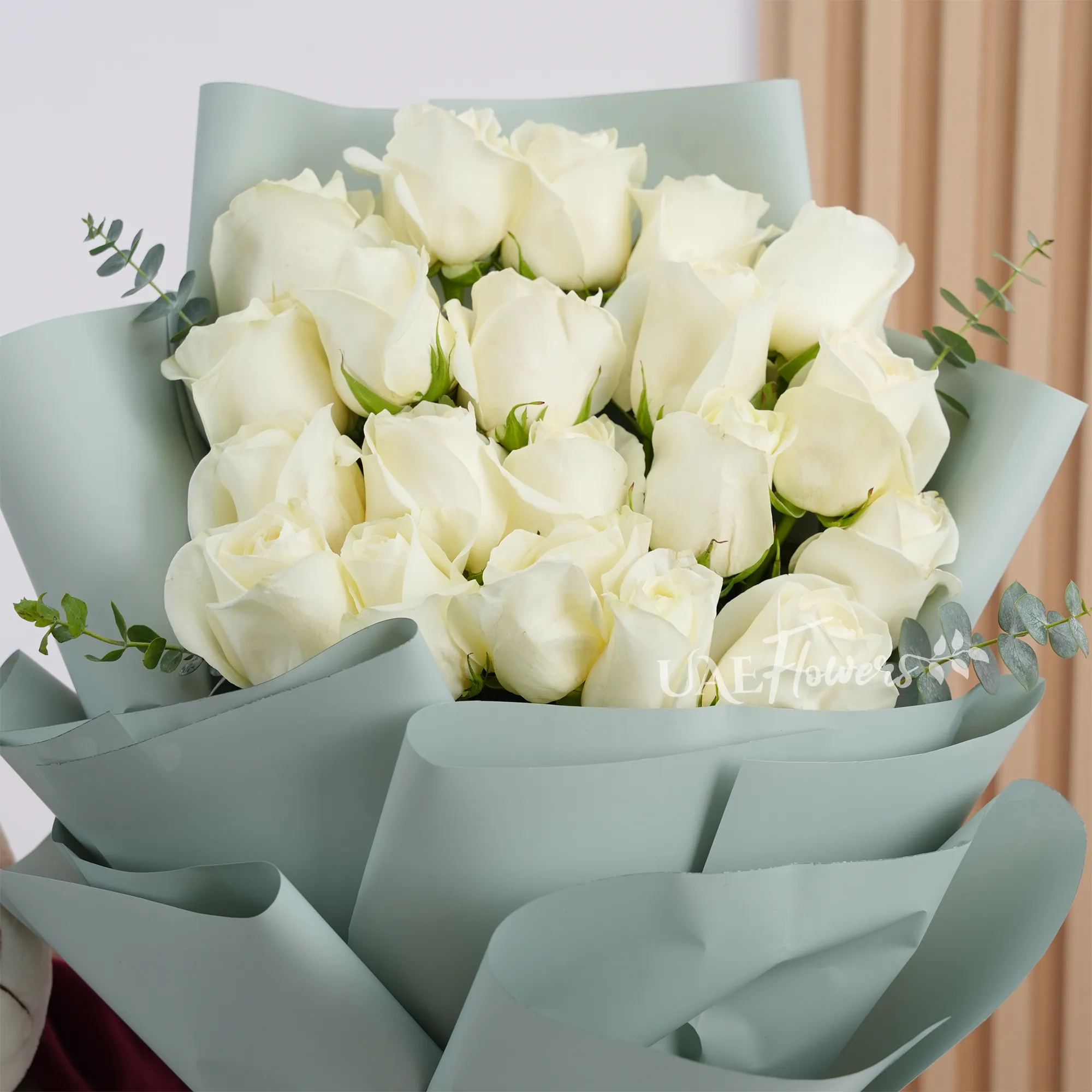 Bouquet of 20 white roses with green fillers wrapped in soft paper and tied with white ribbon, perfect for weddings, anniversaries, and special occasions.