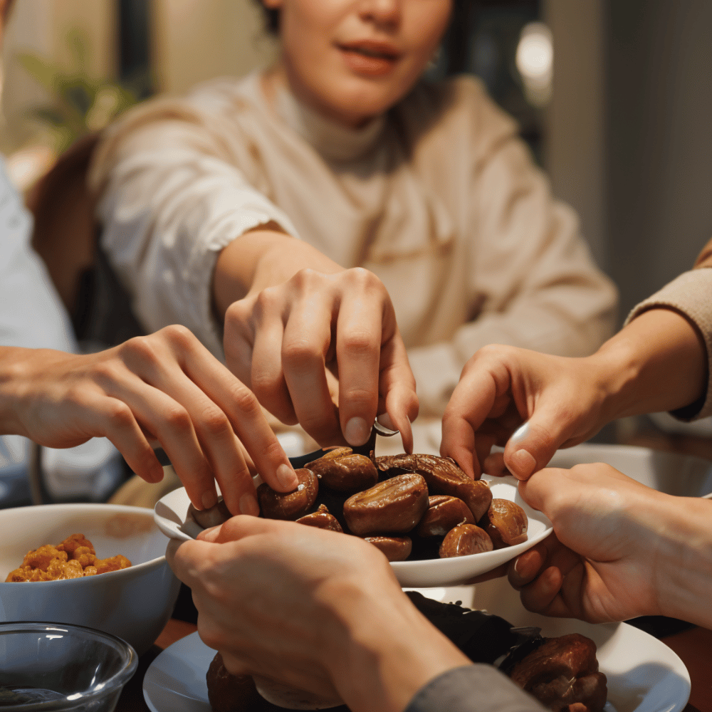 A close-up of multiple hands reaching for dates in a bowl, symbolizing communal breaking of fast during Ramadan.