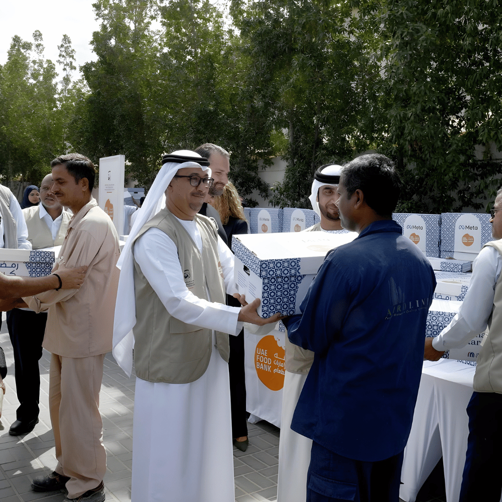 Volunteers in traditional Emirati attire distributing food boxes at a charity event, highlighting Ramadan generosity and giving back.