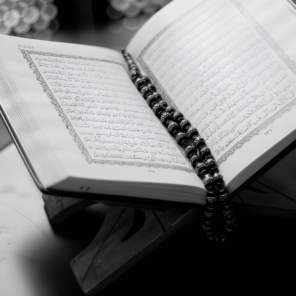 A black-and-white close-up of the Quran with prayer beads resting on it, symbolizing faith and reflection during Ramadan Mubarak